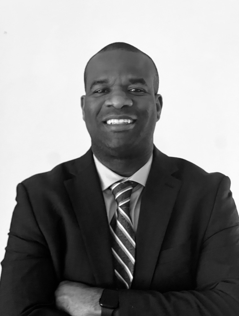Kunle Longe, founder of AI Blueprint Society, smiling with arms crossed in a dark suit and striped tie